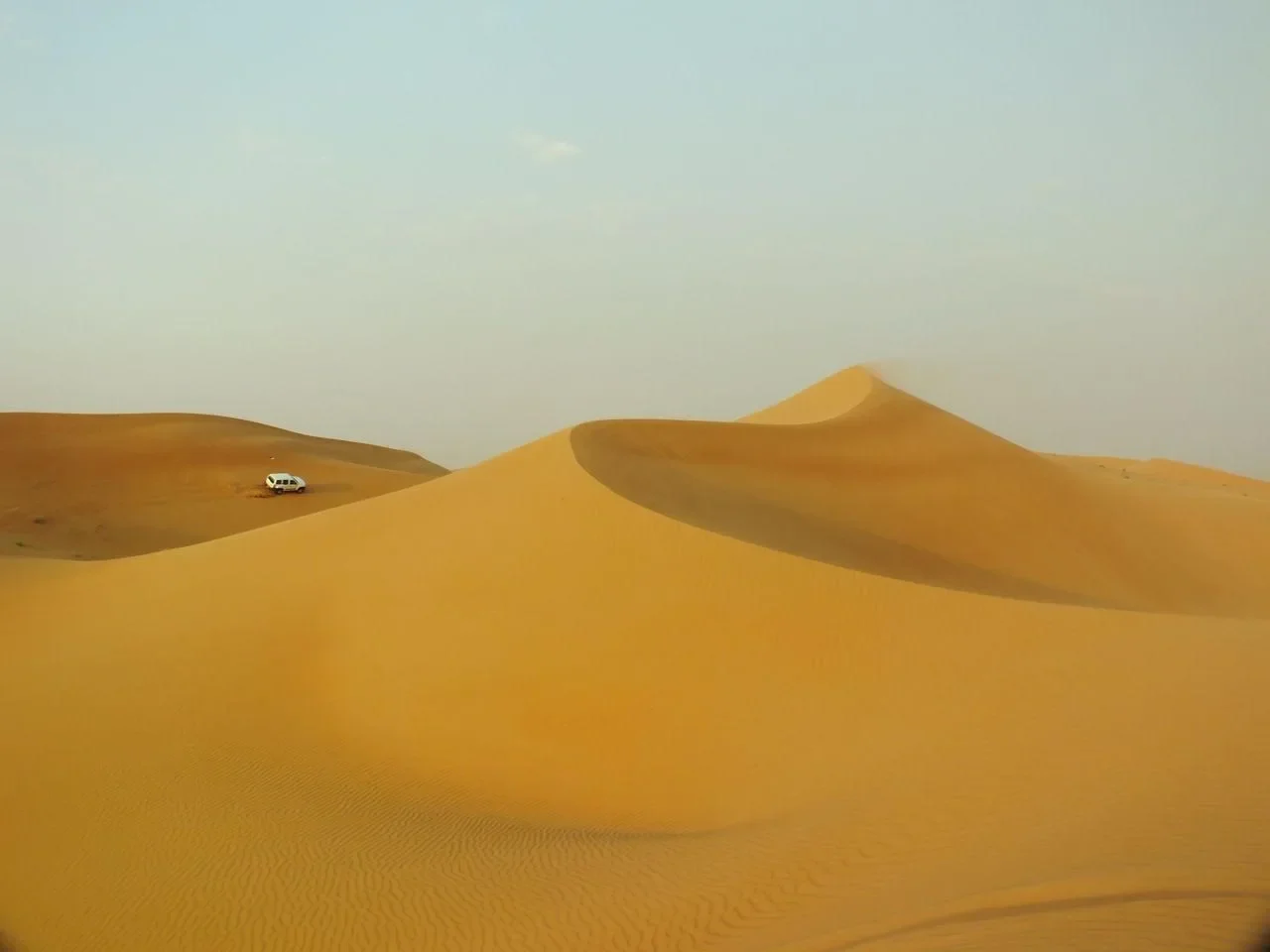 Sweeping dunes of the Arabian Desert with a lone vehicle on a distant ridge